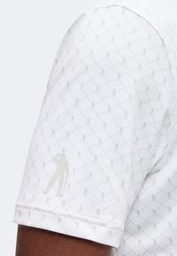 Gros plan d'une manche courte blanche avec un motif subtil de petits golfeurs dans une grille losange répétée sur le tissu.