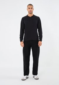 Schwarzes Langarm-Henley-Shirt mit rundem Halsausschnitt und drei Knöpfen, kombiniert mit schwarzen geraden Hosen und Sneakers mit weißen Akzenten.