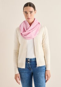 Creme cardigan med ribbede kanter, båret over en hvid top, parret med blå jeans. Lys pink, tekstureret tørklæde viklet om halsen.