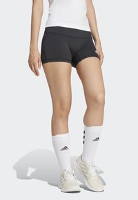 Pantaloni sportivi neri con una cintura larga, cuciture piatte e una vestibilità aderente, abbinati a calze bianche lunghe fino al ginocchio con tre righe nere.