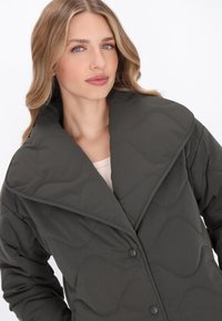 Quiltelt sötétzöld kabát nagy gallérral, hullám mintázattal és gombos záródással. Simább tapintás, alkalmas felső ruházatnak.