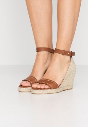 Sandales à talons compensés en cuir marron avec orteils ouverts, présentant un talon en jute tressé et une sangle de cheville. Deux sangles avec une couture blanche en accent.