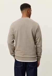 Γκρι φούτερ με στρογγυλή λαιμόκοψη, ριμπ μανσέτες και τελείωμα. Λείο ύφασμα, απλό σχέδιο, φορεμένο πάνω από λευκό πουκάμισο, εμφανίζεται η πίσω όψη.