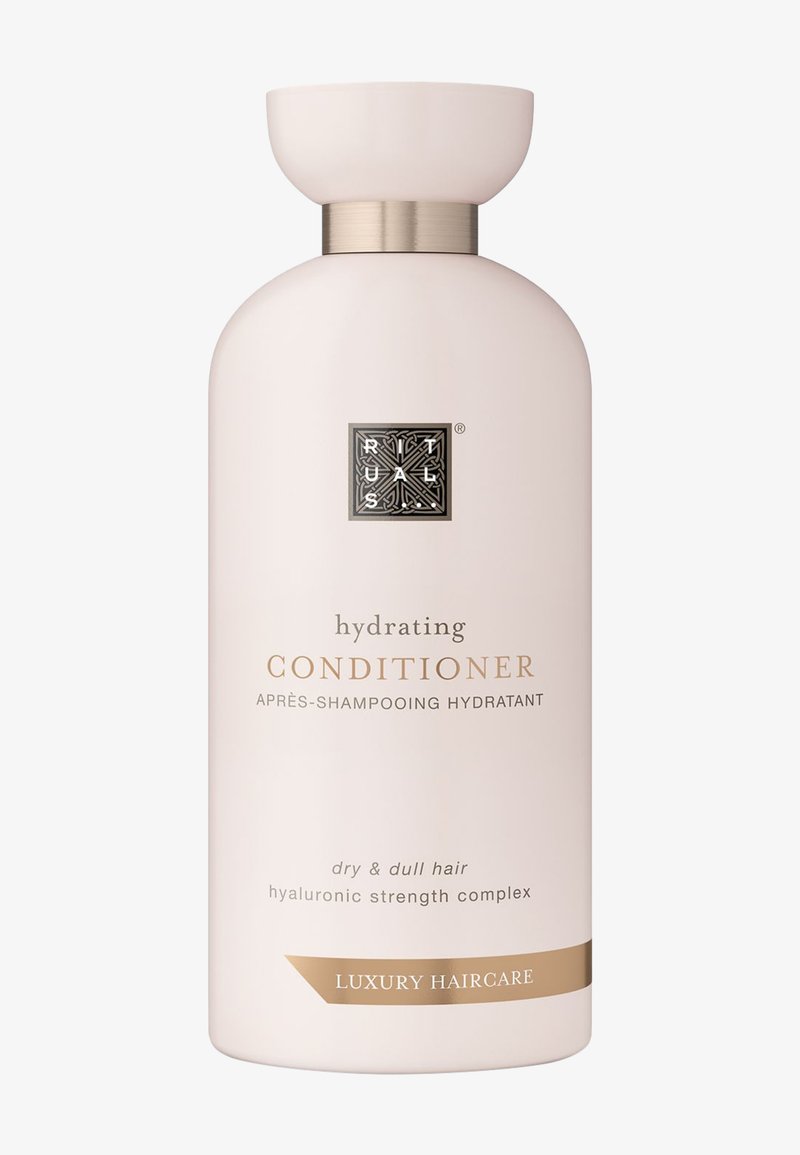 Après-shampooing hydratant dans une bouteille rose pâle avec un accent doré métallique. Présente un logo et des étiquettes en relief à l'avant, destiné aux cheveux secs et ternes.