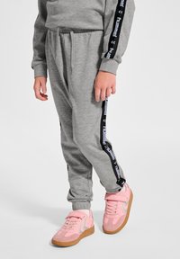 Grå sweatpants har svarta sidosträck med vit "hummel" text. De är kombinerade med rosa sneakers och gummisula, vilket visar upp textur och färger.
