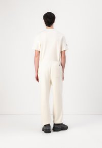 Hvid, kortærmet t-shirt og matchende afslappede bukser med elastisk talje, blødt stof og diskret mærkning på ærmet.