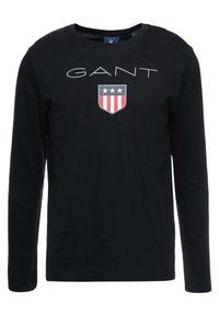 Langärmliges schwarzes T-Shirt aus Baumwolle, mit grauem "GANT"-Logo und einem farbigen Wappen mit roten, weißen und blauen Akzenten auf der Brust.