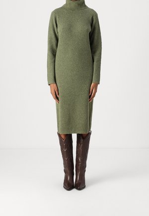 Dzianinowa sukienka golf w kolorze oliwkowej zieleni o długości do kolan, noszona z wysokimi, ciemnobrązowymi kowbojskimi butami ze skóry.