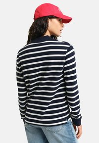 Marineblauwe en witte gestreepte longsleeve shirt met kraag, gecombineerd met lichtblauwe spijkerbroek en een rode pet, met een ontspannen pasvorm.