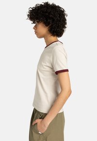 Beige t-shirt met korte mouwen en een maroon kraag en manchetten. Zachte katoen, aansluitend ontwerp en een gladde textuur.