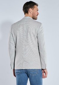 Gray striped blazer with a notched collar, structured shoulders, and buttoned cuffs, paired with blue jeans. Textured fabric detail visible.