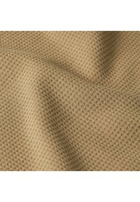 Primer plano de tela beige con textura de punto waffle que muestra pequeños patrones cuadrados uniformemente espaciados y pliegues suaves.