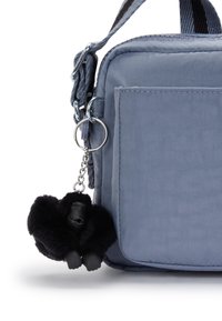 Blå tygaxelväska med frampocket och en svart fluffig gorillanyckelring fäst vid dragkedjan.