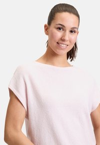 Jasnoróżowa bluzka z krótkim rękawem, wykonana z teksturowanej tkaniny, z dekoltem w łódkę i luźnym krojem, prezentująca gładkie krawędzie i subtelne detale.