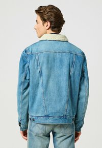 Giacca di jeans blu con colletto in shearling, polsini con bottoni e cuciture visibili. Design pulito con una vestibilità leggermente rilassata.