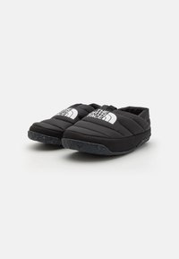 Scarpe slip-on nere, trapuntate, con suola in gomma testurizzata e un logo bianco su ciascun lato. Il morbido materiale superiore offre comfort e calore.