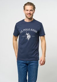 Marineblaue Baumwoll-T-Shirt mit Rundhalsausschnitt, ausgestattet mit weißen Text und einer Grafik eines Polo-Spielers. Kurze Ärmel, legere Passform.