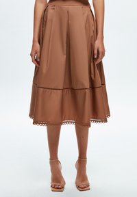 Jupon midi marron en tissu lisse, avec des plis, une forme évasée et un détail en dentelle au bas. Associé à des sandales à lanières nude.