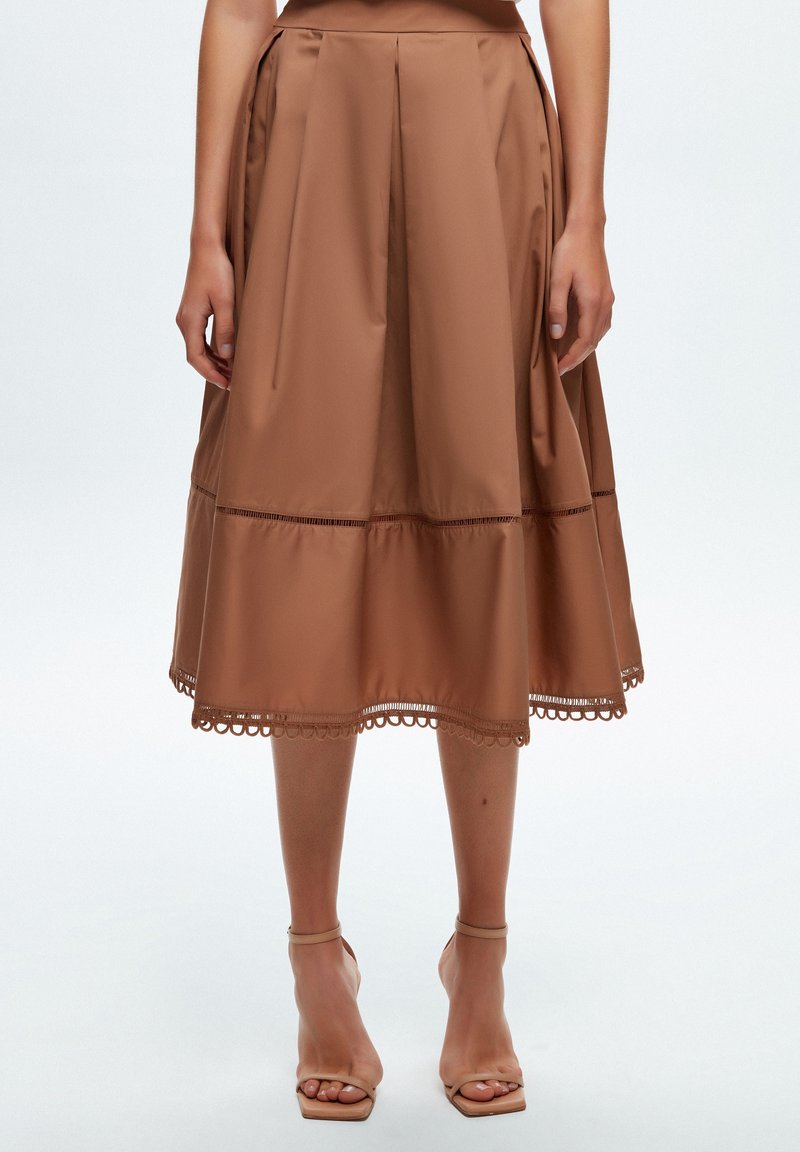 Jupon midi marron en tissu lisse, avec des plis, une forme évasée et un détail en dentelle au bas. Associé à des sandales à lanières nude.