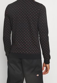 Black sweatshirt featuring a small, repeating burgundy floral pattern, ribbed cuffs, and hem. Made from a soft, textured material.