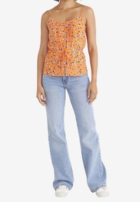 Orange ärmlös topp med blommönster, samlad design, justerbart band i midjan; ihopkopplad med ljusblå utsvängda jeans och vita sneakers.