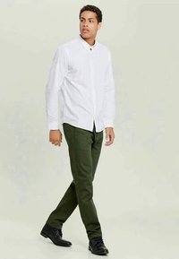 Chemise blanche à manches longues et à boutons associée à un pantalon chino vert foncé et des chaussures noires. La chemise a un col et une texture subtile.