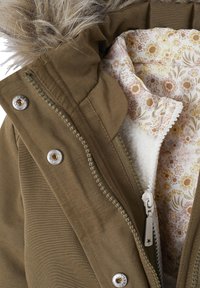 Olivgrüne Parka mit Kunstfellkapuze, ausgestattet mit metallischen Druckknöpfen, Reißverschluss und einem floral gemusterten Futter mit weicher Textur.