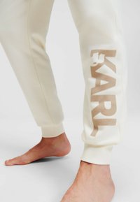Crèmekleurige joggers van zacht materiaal, met een groot, lichtbruin "KARL"-logo op het linkerbeen en geribbelde boorden bij de enkels.