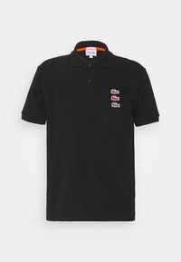Black polo shirt made of cotton, featuring a collar and three embroidered crocodile logos in red, brown, and green on the left side.