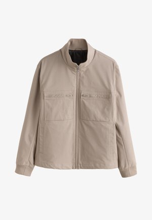Beige Jacke mit Reißverschluss, Stehkragen, zwei Reißverschlusstaschen auf der Brust und langen Ärmeln.