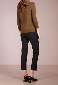 Pull en tricot marron à manches trois-quarts avec fentes latérales, associé à un pantalon noir ajusté et des ballerines en cuir verni noir.