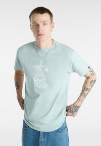 Camiseta de color verde menta clara hecha de tela suave, con un gráfico de un conejo de dibujos animados en blanco y el texto "vans". Mangas cortas, corte relajado.