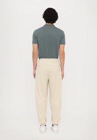 Kortebroek, donkerblauwe polo met witte accenten, gecombineerd met crèmekleurige, ontspannen pasvorm broek en witte sneakers.