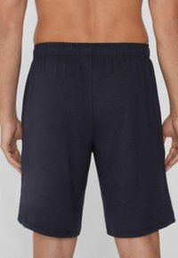 Námořnické modré sportovní šortky vyrobené z měkké tkaniny, s elastickým pasem a hladkým povrchem, končící těsně nad kolenem.