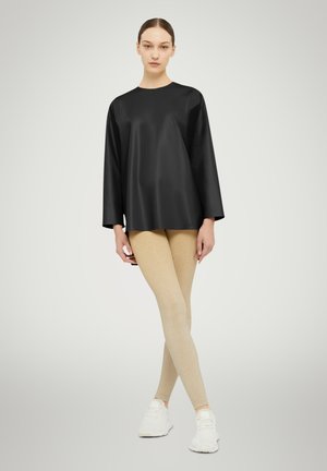 Top nero a maniche lunghe in un tessuto liscio abbinato a leggings beige lucidi. La modella indossa scarpe da ginnastica bianche. Design semplice e moderno.