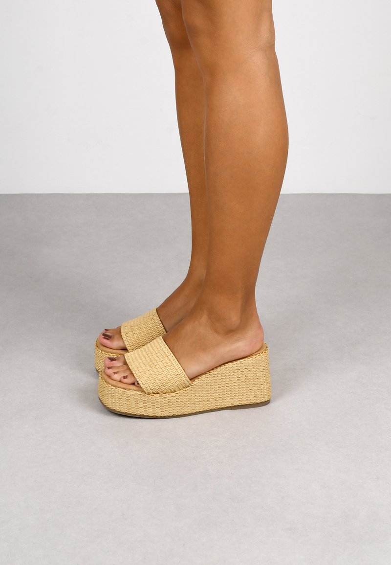 Las sandalias de plataforma trenzadas en color beige presentan correas anchas en la parte superior, una superficie texturizada y un tacón de cuña resistente.