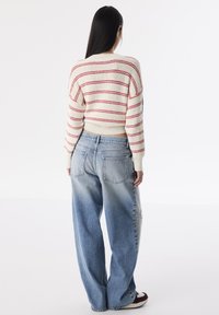 Maglione a maglia di colore crema con strisce rosse, abbinato a jeans in denim leggero oversize di colore blu con dettagli sfrangiati.