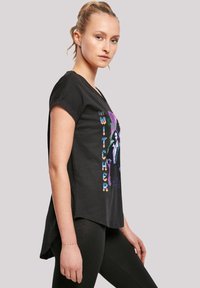 Black short-sleeve t-shirt featuring a colorful graphic print of "The Witcher" on the front. The shirt has a loose fit and curved hem.