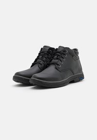 Botas de cuero negras hasta el tobillo con un acabado suave, punteras redondas, diseño de cordones y forro gris. Cuenta con una suela acolchada con acento azul.