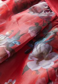 Tejido floral rojo con grandes flores en estilo acuarela en tonos de púrpura, azul y rosa, con una textura suave y transparente y detalles fruncidos.
