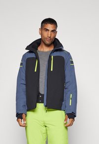Chaqueta de hombre con una combinación de colores azul y negro, con detalles en verde, capucha, múltiples bolsillos con cremallera y una textura suave.