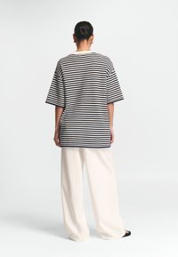 Triibuline ülikoošhede t-särk tumesinisest ja kreemilisest värvist, lühikeste varrukatega, ümmarguse kaelusega, koos kreemiliste laiade pükstega ja mustade libisevate kingadega.