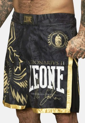 Pantaloncini da arti marziali neri e dorati con testo "LEONE", emblema del leone e mano tatuata che tiene il lato.
