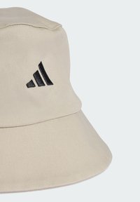 Beige bucket hat made of textured fabric, featuring a black embroidered logo on the side and a wide, downward-sloping brim.