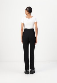 Pantaloni neri su misura con vita alta, caratterizzati da una trama liscia e tasche laterali, abbinati a una blusa fitted bianca a maniche corte.