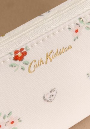 Biely textil s malými kvetinovými vzormi, zlatým logom "Cath Kidston" a bielym zipsom pozdĺž hornej hrany.