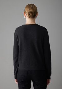 Black, textured sweater with long sleeves and a rounded neckline. The model wears it with dark trousers, shown from the back against a neutral background.