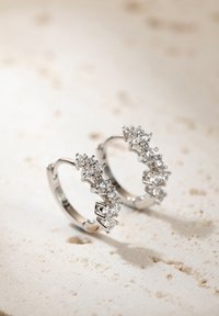 Boucles d'oreilles en argent avec un design ondulé, comportant plusieurs pierres précieuses rondes et transparentes serties en griffes.