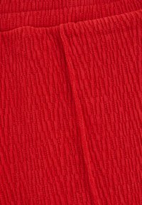 Texturovaná červená tkanina s ryhovaným vzorom, ktorá predvádza jemný, vláknitý vzhľad a mierny lesk na povrchu.