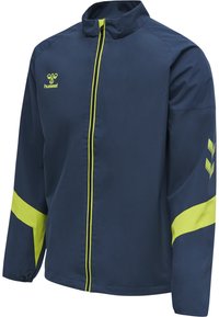 Marinblå sportjacka med starkt gula detaljer, hel dragkedja, hög krage och logotyp. Har långa ärmar med kontrasterande axeldesign.